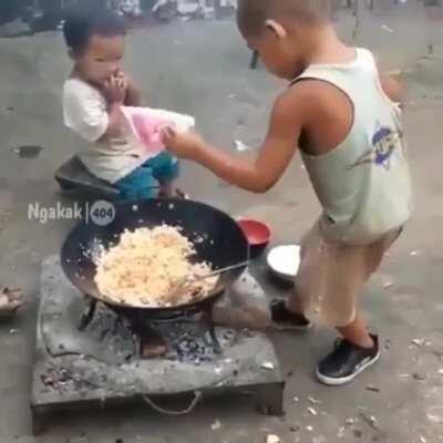 Toddler cooks food for his little sister