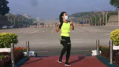 A woman conducted her aerobics class in Myanmar without realizing a coup was taking place. Behind her, a military convoy arrives at parliament.