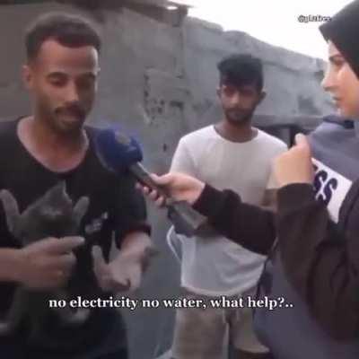 Palestinian man talks to press while comforting a little cat clinging on to his shirt 