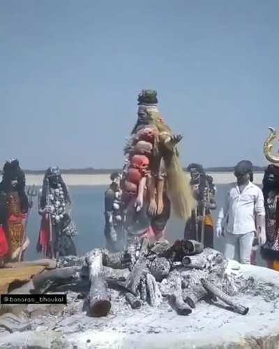 An Indian Aghori performing a ceremonial dance over funeral pyre whilst wearing a garland of human skulls and severed arms of corpses.