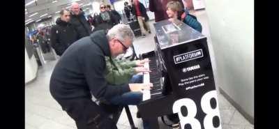 Random guy, joins other random guy in playing the piano.