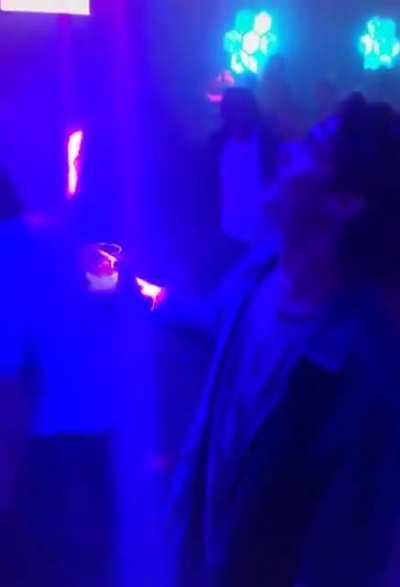 This guy lines his drink up with a light in a club perfectly