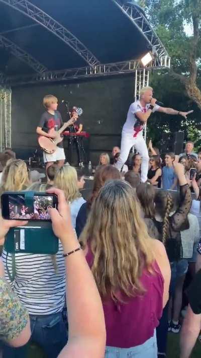 A rock band is performing and the singer sees a kid with a banner asking to play guitar with them. The singer asks him:  - Do you really know how to play guitar? - Yeah! - What’s your favorite band? - Guns N’ Roses  What happens next is incredible!