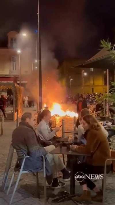 French diners enjoy wine as fire lit by protesters burns nearby