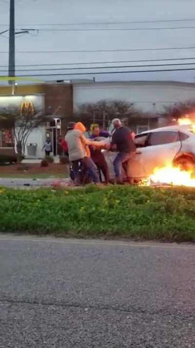 Bystanders with no protective gear pull a woman from a car engulfed in flames