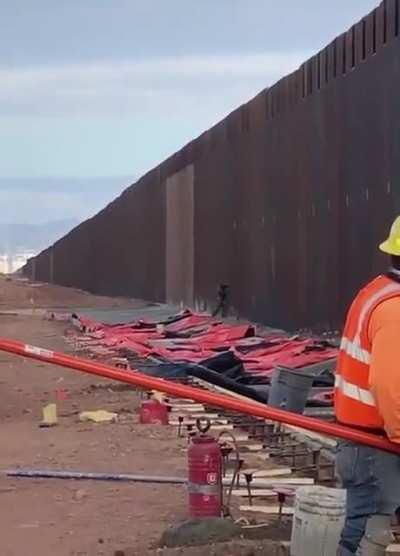 man climbs the US - Mexico border while people are working on it