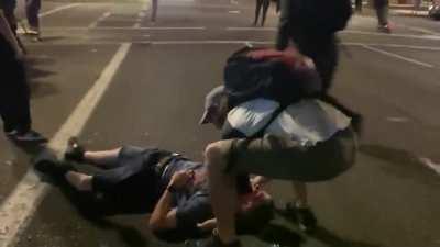 Rioters in downtown Portland detain man who had a car crash. They force him to sit on the ground while they search his belongings. One of them runs up and kicks him in the head, instantly knocking him out.