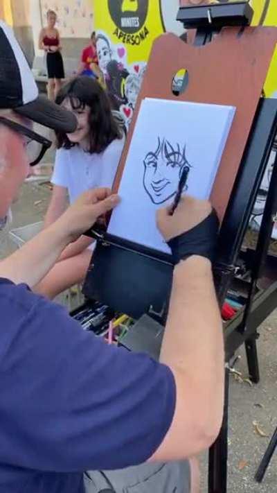 A street artist draws a cartoon version of a girl.