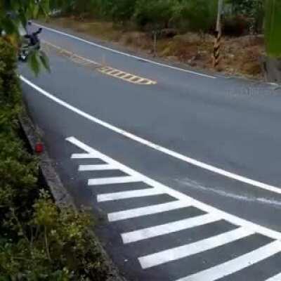 Motorcycle skids at the curve to the other lane and gets hit with another bike, sending the rider flying.