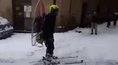 Guy is wearing a backpack with a propeller motor and a pair of skis