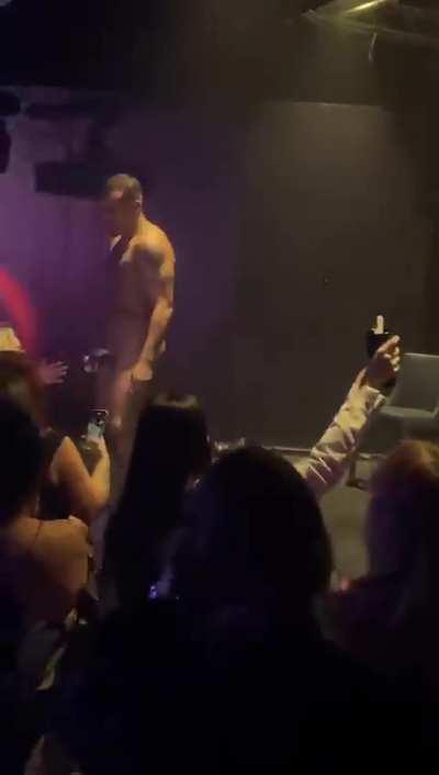 Women in crowd licking male stripper's big cock.