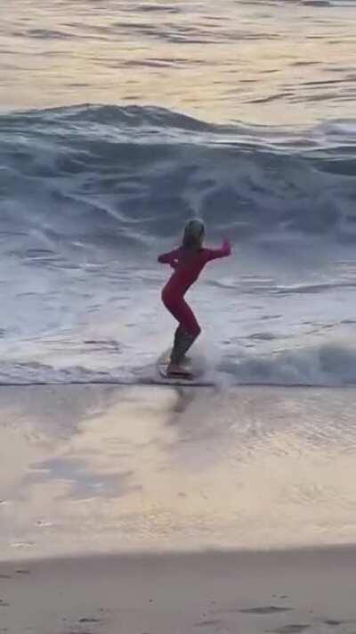 Young girl uses a skipboard to hit a wave and do a flip in the air