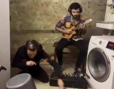 Playing a techno track using a washing machine and a bucket as part of their tools