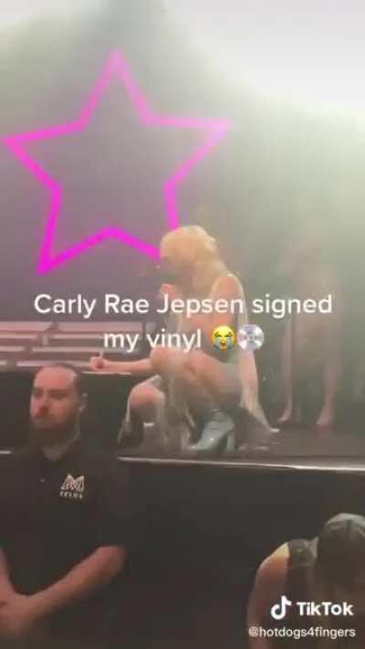 Carly Rae Jepsen signing a record for a fan in the middle of performing a song