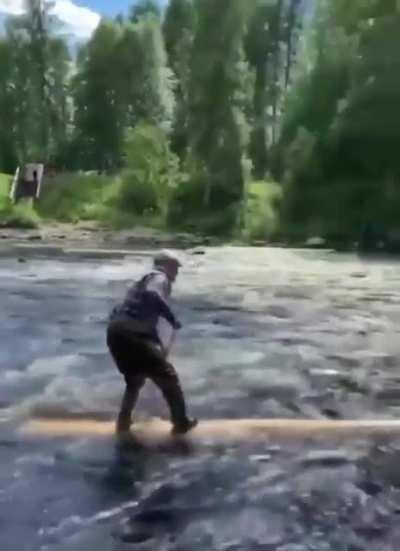 An old man riding and paddling on a log downstream and making it look easy