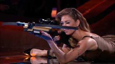 Nicole Scherzinger hitting the bullseye with a Crossbow while doing the splits.