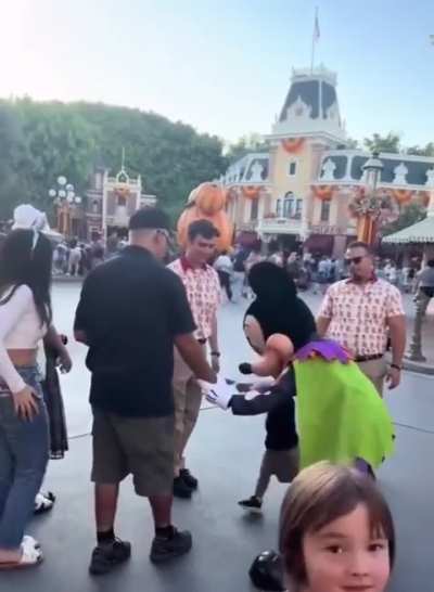 Toddler gets bowled over by Mickey Mouse, who admonishes the dad for not keeping a hold of his kid