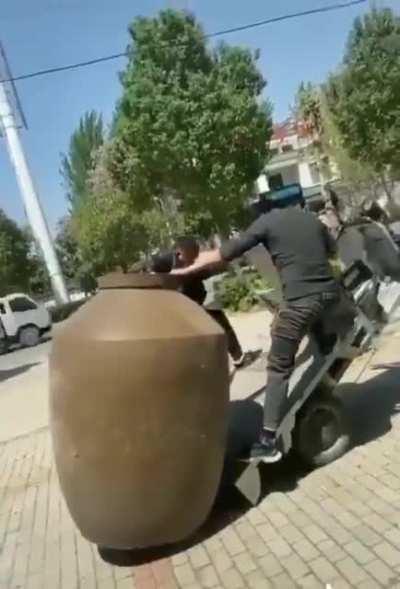 Couple of geniuses trying to put a huge jar onto a small tricycle