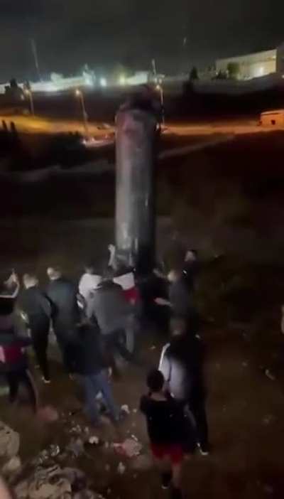 Palestinians in the West Bank collect a rocket shroud and celebrate with pictures. 