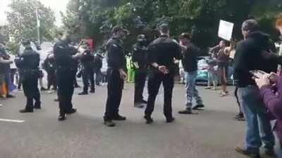 Policeman in Oregon flashing a white power sign at a Proud Boy