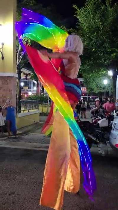 Person on stilts celebrating pride with rainbow colored veils.