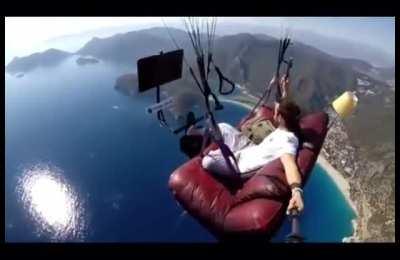 Man paraglides on a couch and watches tv