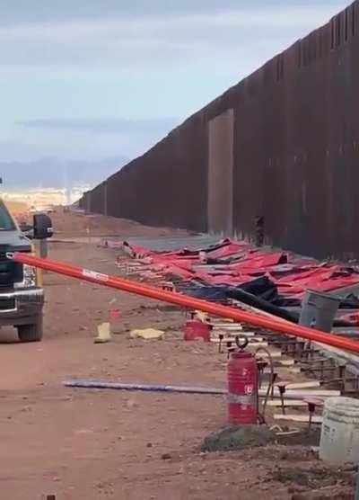 man climbs the US - Mexico border while people are working on it