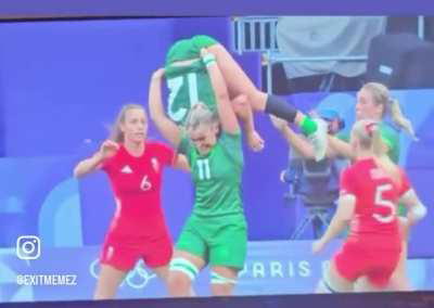 Woman on the Ireland Rugby team picking up one of her teammates by her shorts to catch the ball