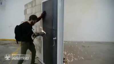 The Hacksmith uses a wrist mounted plasma torch to cut through a steel door.