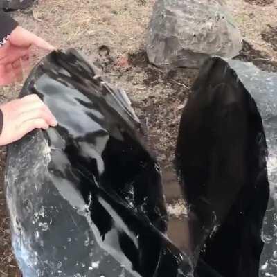 An Obsidian stone split in half. Obsidian is a natural volcanic glass formed when lava high in silica cools quickly, preventing crystal growth.