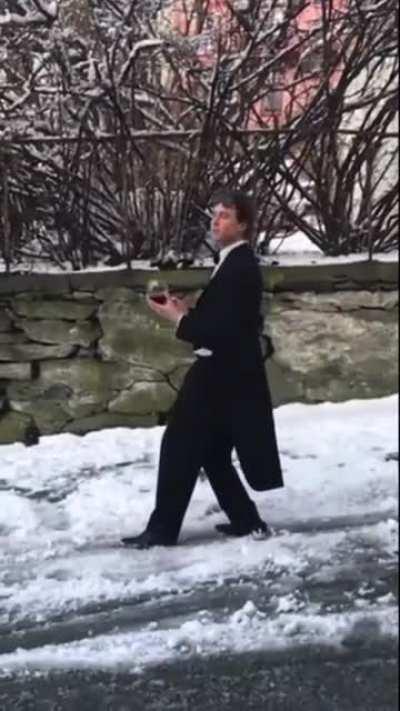 Guy slides down hill with a tuxedo with a glass of wine while on the phone