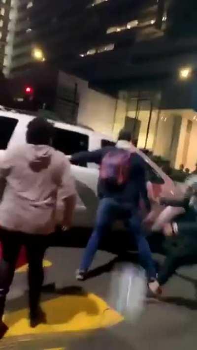 Guy stands behind a car as other people attack it from the front