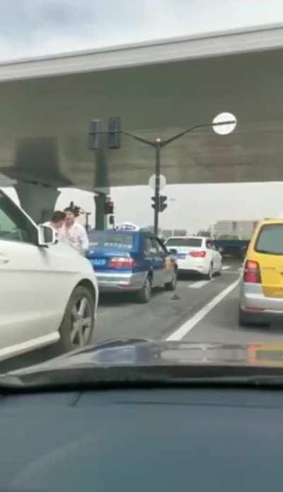 Two dudes fighting in stopped traffic.