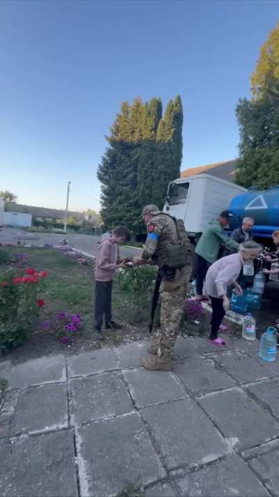 A Ukrainian soldier gives food to a child while people nearby calmly water. The locals are grateful because the russian authorities have left them to their own devices.