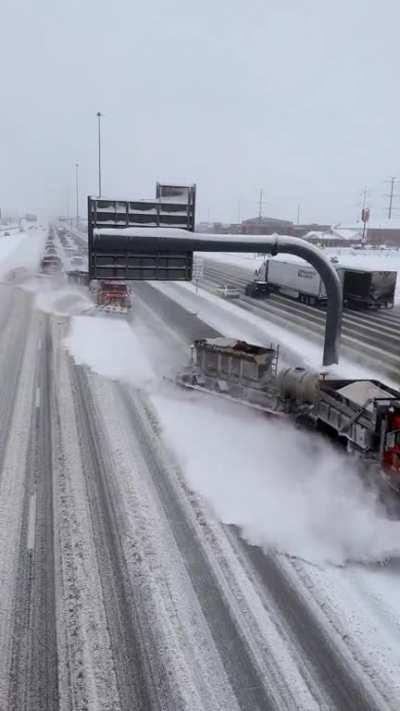 Team of plows with attached tow plows clearing snow from multiple lanes.