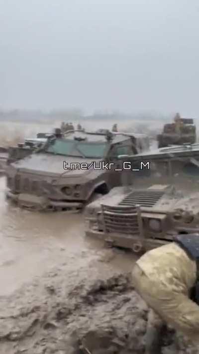 Ukrainian vehcles stuck in deep mud being dug out amidst falling snow.