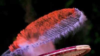 A tennis racquet covered in powder hit with a ball in slow motion