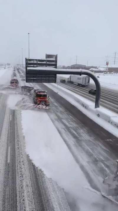 Team of plows with attached tow plows clearing snow from multiple lanes