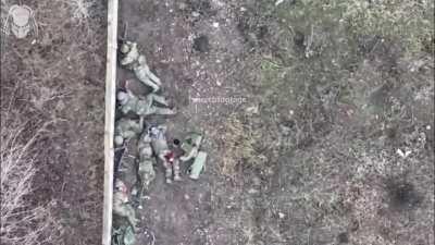 Ukrainian drone drops explosive next to Russians taking cover behind a wall. Shrapnel can be seen hitting the wall.