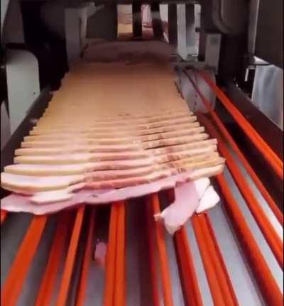 A machine chopping raw pork into bacon