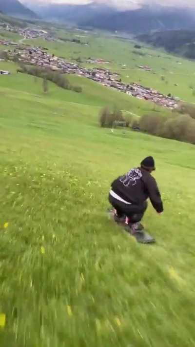 A guy slides down the mountain on a board on the grass