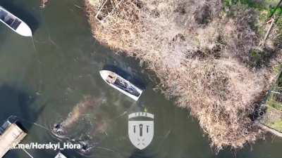 Two Russian soldiers on a boat in civilian clothing are hit with an accurate drone dropped grenade strike injuring them and igniting the fuel, they manage to swim to shore but can be seen bleeding heavily.