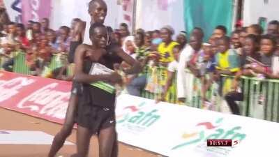 Simon Cheprot demonstrating sportsmanship of the highest order helping competitor Kenneth Kipkemoi cross the finish line first in the Okpekpe International 10-kilometer Road Race, giving up Gold in the process