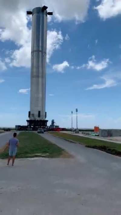Musk taking a walk next to Booster 4 roll out ( black shirt and hat )