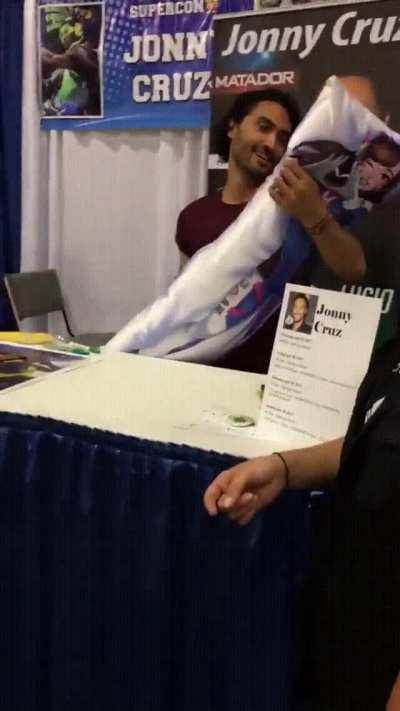 The Lucio voice actor Johnny Cruz receives a Dva body pillow from a fan.