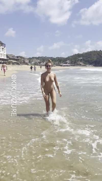 Naked on a beach while people are wearing suits