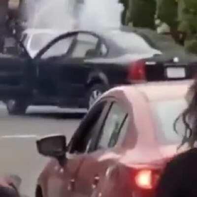 LA rioter lights firework on the street. Gets it thrown back into his car.