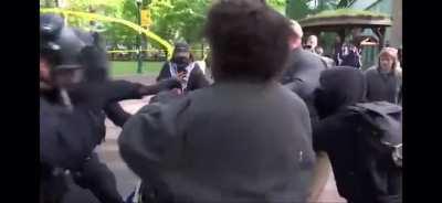 Student Protestor attempts to charge into a police officer with a trash can riot shield. 