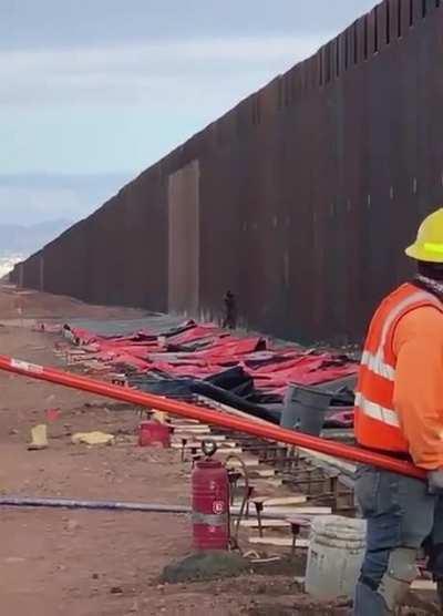 man climbs the us - mexico border while people are working on it