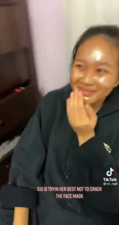 Girl entertained by her sister trying not to move her face with a beauty mask on